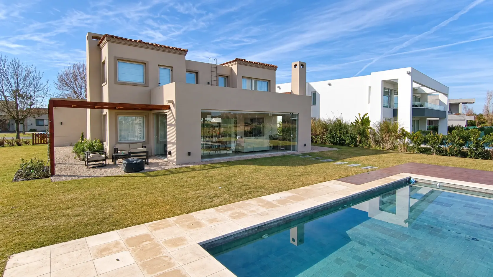 Casa con quincho cerrado con paños de vidrio frente al jardín y la piscina