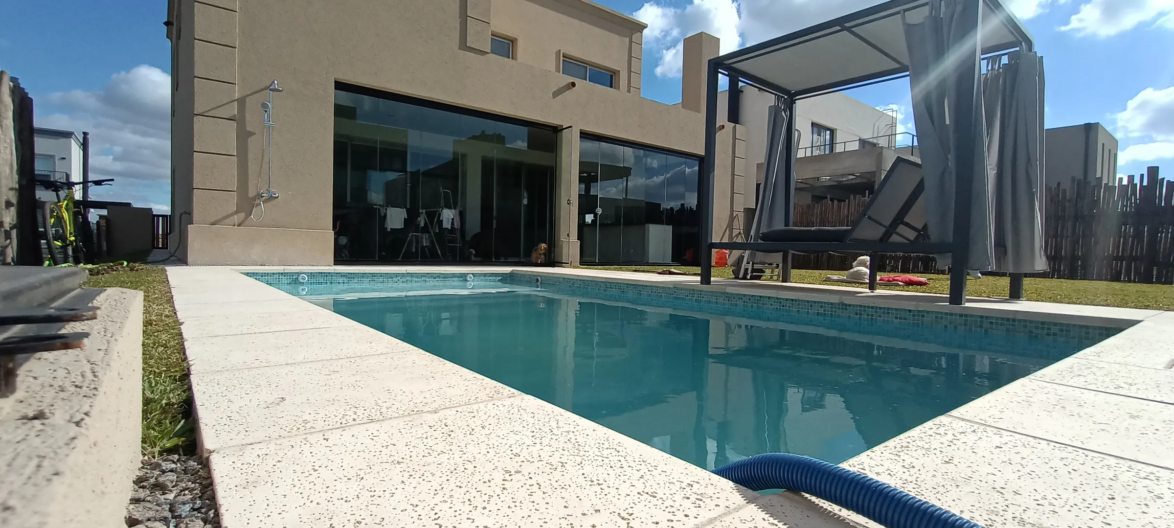 Planta baja cerrada con vidrio junto a la piscina y una pérgola con toldo