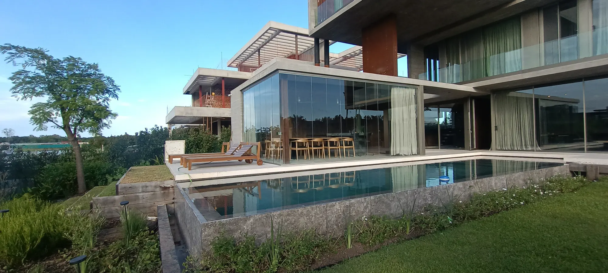 Galería vidriada con comedor exterior junto a una piscina