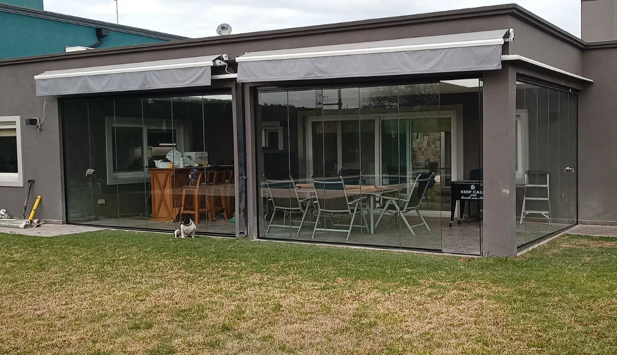 Quincho con cerramiento de vidrio y toldo, visto desde el jardín